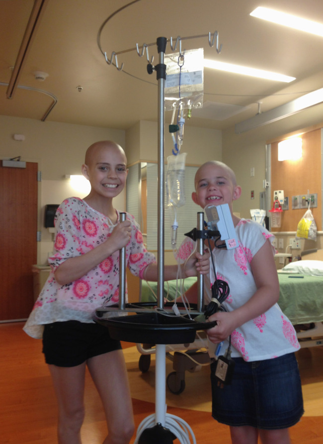 Delaney Clements (left), 11, and Kamryn Renfro, 9, stand together at a hospital in Colorado. Kamryn was suspended from her school because having a shaved head goes against the school’s dress code.   AP-Yonhap