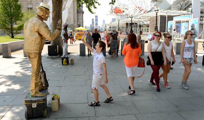 A busker (left) entertains tourists in front of the London Eye in London in 2012.   AFP-Yonhap