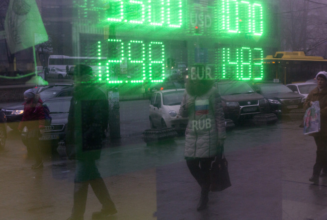 Pedestrians are reflected in the window of a foreign currency exchange store advertising its rates in Kiev, Ukraine.   Bloomberg