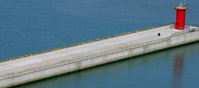 Yellow ribbons hung by people wishing for the safe return of the missing passengers blow in the wind as a person sits alone on the seawall on Jindo Island on Thursday.
Yonhap
