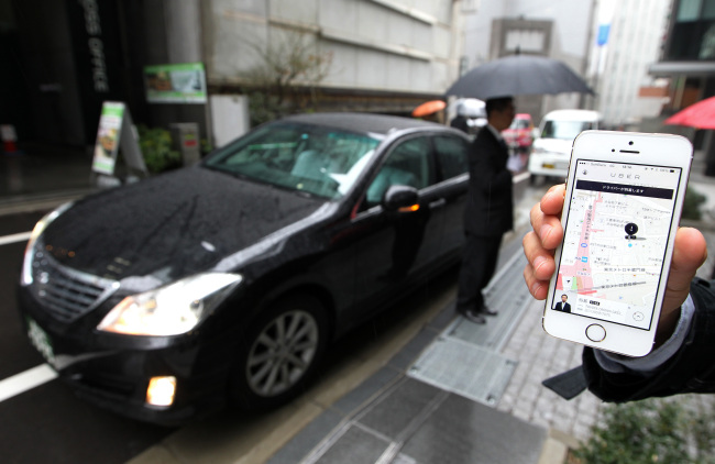 An Uber Japan employee holds an iPhone 5S showing a map on the Uber application during a demonstration in Tokyo in March. Uber Technologies Inc. is a booking-app developer backed by Google’s investment arm and Amazon.com founder Jeff Bezos.   Bloomberg