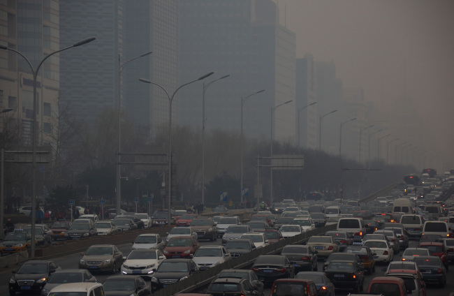Traffic moves along a street shrouded in haze in Beijing.     Bloomberg