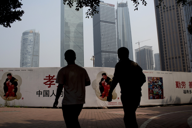 Two pedestrians are seen in front of a public service advertisement promoting the “Chinese Dream” slogan unveiled by President Xi Jinping in the Zhujiang New Town district of Guangzhou, China.   Bloomberg