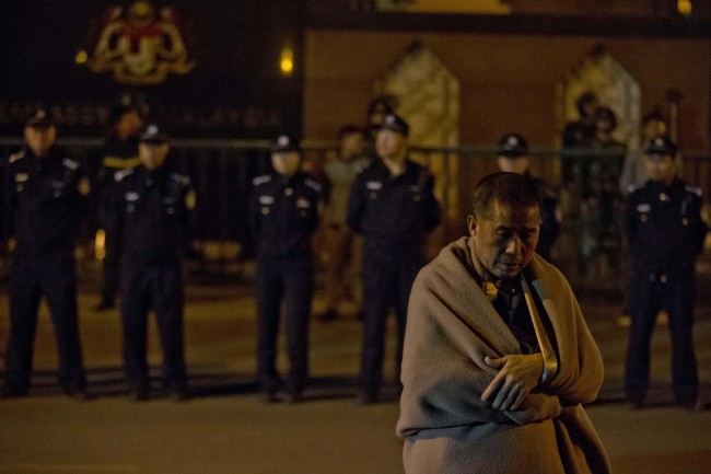 A relative of Chinese passengers onboard the Malaysia Airlines MH370 wrapped in a blanket against the cold, waits for embassy staff to meet their demands outside the Malaysian Embassy in Beijing.   AP-Yonhap
