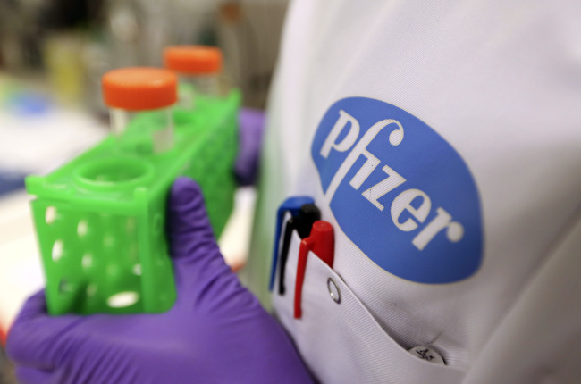 A Pfizer logo sits on the lab coat of an employee at the research laboratory of Neusentis Ltd., a unit of Pfizer Inc., in Cambridge, England.   Bloomberg
