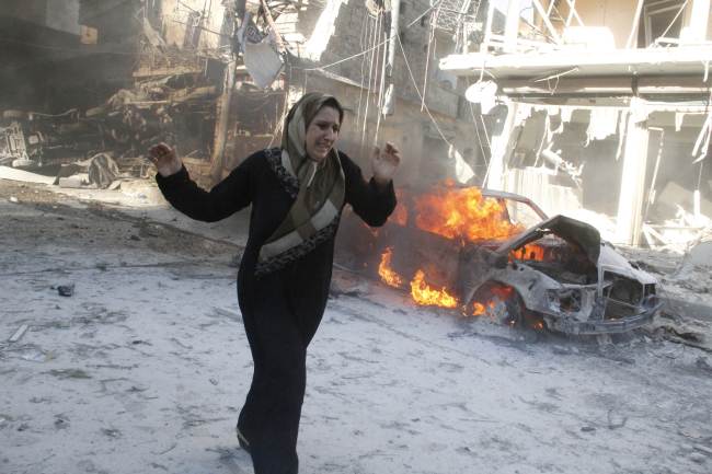 A Syrian woman walks past the burning wreckage of a car following reported air strikes by government forces  in the Halak neighborhood in northeastern Aleppo, Syria, Thursday.   AFP-Yonhap