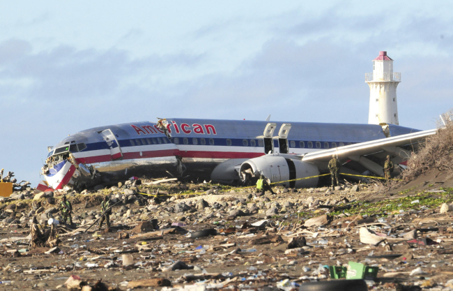 Workers sift through debris surrounding the fuselage of American Airlines Flight AA331, which crash-landed overnight on a flight from Miami to Jamaica on Dec. 23, 2009.   AP-Yonhap