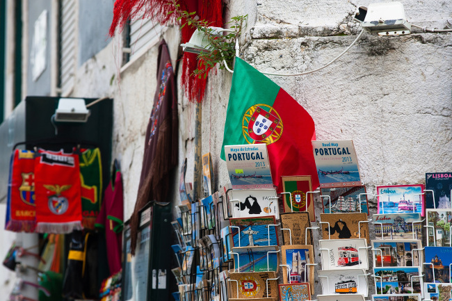 A Portuguese national flag hangs above a display of postcards and tourist guide books outside a souvenir store in Lisbon.   Bloomberg