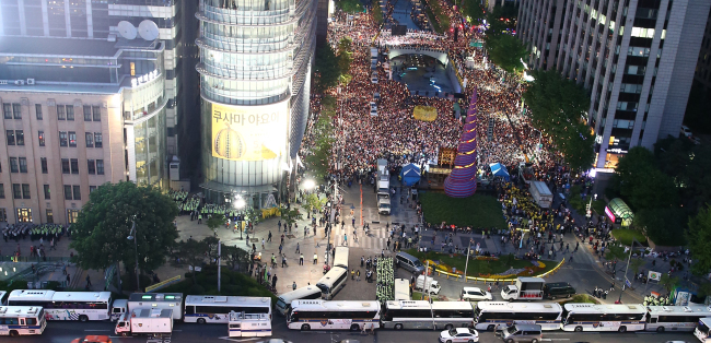 Citizens hold a candlelight vigil in memory of the victims of the Sewol ferry disaster in Cheonggyecheon Square in Seoul on Saturday with police buses surrounding the area.   Yonhap