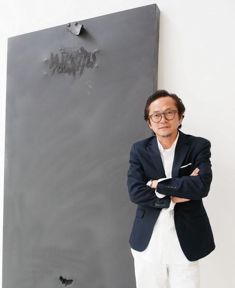 Artist Jeong Jai-young poses for a photo in front of one of his paintings at his studio in Busan.   (Lee Woo-young/The Korea Herald)