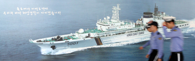 Maritime policemen pass by a patrol-vessel picture on a wall at the Korea Coast Guard on Monday, when President Park Geun-hye said the administration would dismantle the agency in the wake of the Sewol disaster.   Yonhap
