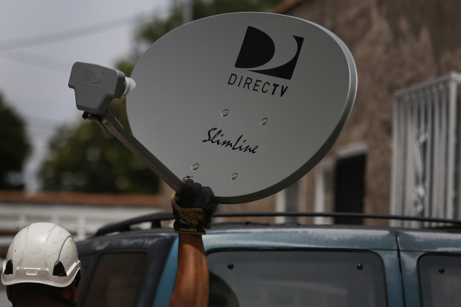 A DirecTV technician carries a new satellite TV dish while performing an installation in Lynwood, California.   Bloomberg