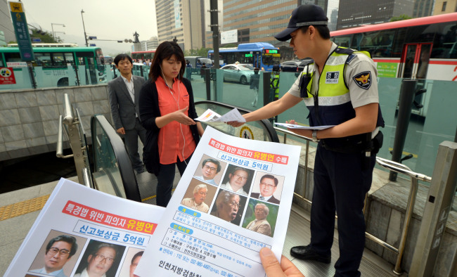 A policeman hands out posters of the wanted Yoo Byung-eon and his eldest son Dae-gyun to passersby in downtown Seoul on Monday.   Kim Myung-sub/The Korea Herald