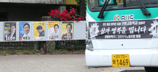 Posters of Ansan’s mayoral candidates in the June 4 elections are shown next to a city bus carrying “rest in peace” banner in Ansan, Gyeonggi Province, Sunday. The Sewol’s sinking killed more than 240 students from the city’s Danwon High School.   Yonhap