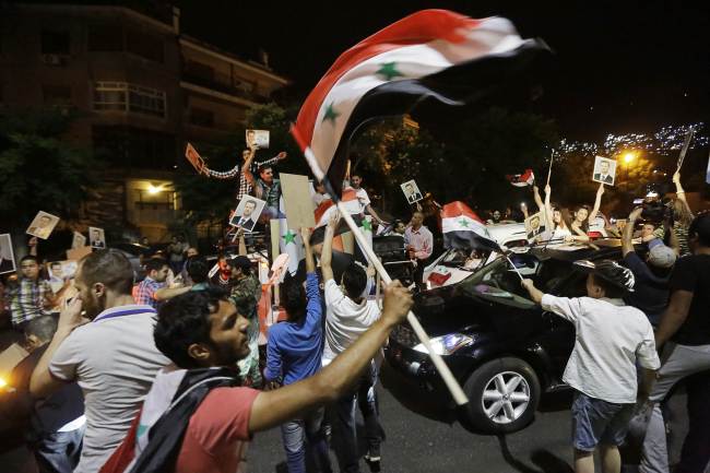Syrians wave national flags and hold pictures of Syrian President Bashar Assad after he was announced the winner of the country’s presidential election in Damascus on Wednesday.   AFP-Yonhap