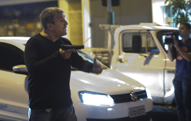 A man who identified himself as a police officer points his gun at anti-World Cup protesters blocking a road that leads to the Maracana stadium in Rio de Janeiro, Brazil, Sunday.   AP-Yonhap