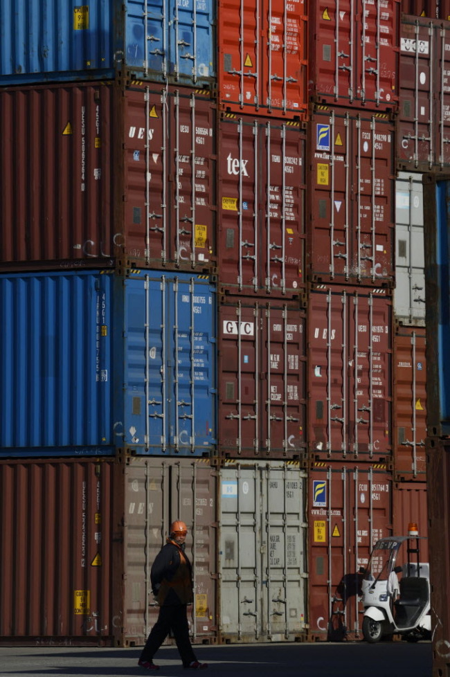 A worker walks past stacked containers at a shipping terminal in Yokohama City, Japan.   Bloomberg
A worker walks past stacked containers at a shipping terminal in Yokohama City, Japan.   Bloomberg