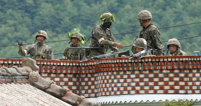 Armed troops keep a watch on the rooftop of a civilian house as a sergeant, who killed five soldiers and wounded seven others in a shooting rampage Saturday, engaged in a firefight in Goseong, Gangwon Province, Sunday.   Yonhap
