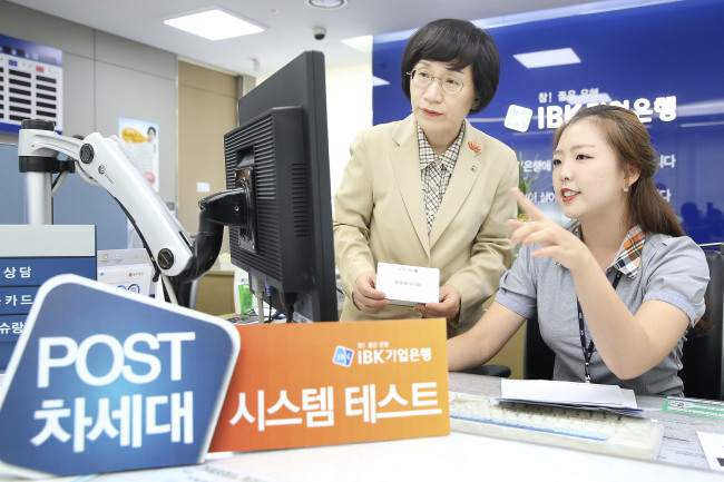 Kwon Seon-joo (left), CEO of Industrial Bank of Korea, looks at a computer screen at one of the bank’s branches in Gyeonggi Province during a trial run for the bank’s new IT system Saturday.   IBK