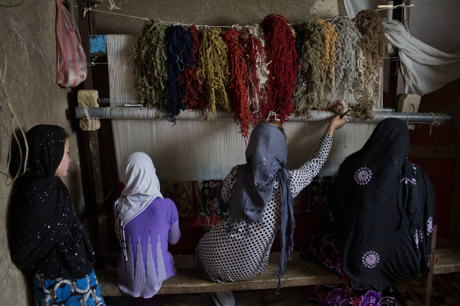 Women weave a carpet on a loom at their home in the neighborhood of Kata Belandi, south of Kabul, Afghanistan. (Bloomberg)