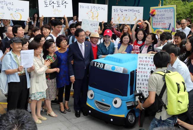 The Seoul mayor poses with citizens and a miniature of the Tayo Bus, a bus based on a popular anime character targeting children, after the inaugural ceremony at City Hall on Tuesday.   Yonhap