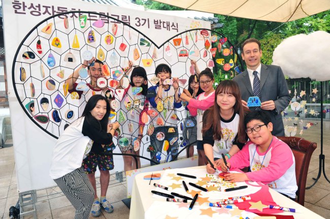 Han Sung Motor CEO Ulf Ausprung (right) and art students of the company’s “Dream Gream Project” pose next to their work titled “Dynamic: Connecting the Hearts” during an event celebrating the program’s third anniversary at Korea House in Pil-dong, central Seoul, June 23.   Han Sung Motor
