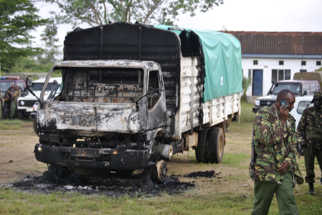 Policemen stand near the wreckage of a burned vehicle after gunmen attacked outside Gamba police station in Gamba, Kenya, Sunday.   AP-Yonhap