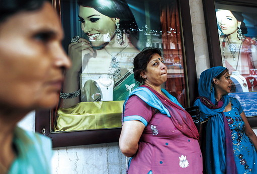 Women stand beside advertisements for jewelry during the festival of Dhanteras, two days before Diwali, in the Zaveri Bazaar area of Mumbai, India. (Bloomberg)