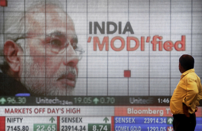 A man looks at a screen showing television coverage of Indian Prime Minister Narendra Modi and the latest figures for the S&P BSE Sensex and the CNX Nifty index at the lobby of the Bombay Stock Exchange in Mumbai.   Bloomberg