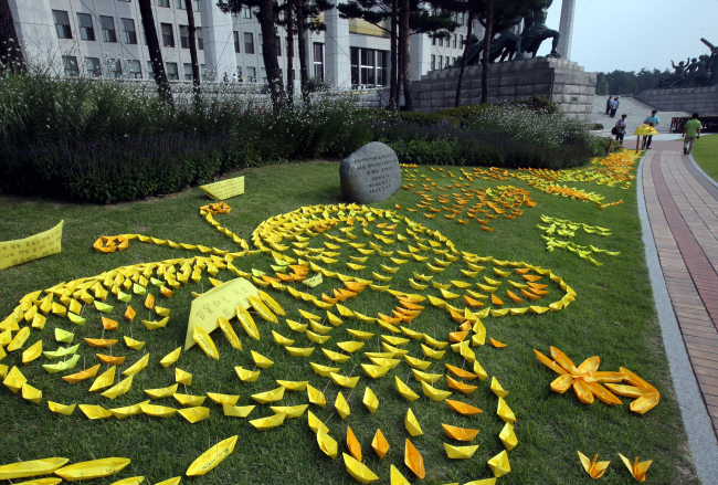 Yellow paper boats symbolizing the April 16 Sewol ferry disaster are arranged in various formations on a lawn outside the National Assembly on Monday.   Lee Gil-dong/The Korea Herald