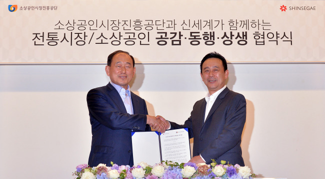 Shinsegae Group president Kim Hae-sung (right) shakes hands with Lee Il-kyoo, chairman of Small Enterprise and Market Service, after signing an agreement promising 10 billion won ($9.7 million) of support from the retail giant over five years for the growth of traditional markets, at the Korean Chamber of Commerce and Industry in Seoul on Wednesday.   Lee Sang-sub/The Korea Herald