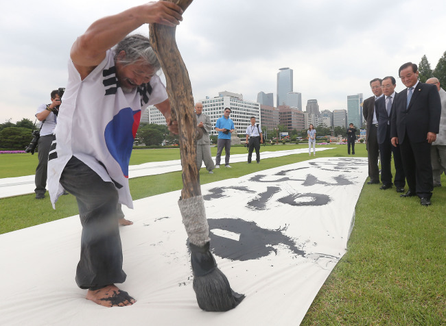 Calligrapher Kim Dong-wook writes “The Republic of Korea is a democratic republic,” which is Article 1 of the nation’s Constitution, on a large cotton cloth in front of the National Assembly in celebration of Constitution Day in Seoul on Thursday.   Yonhap