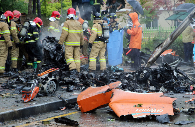 Rescuers work near the wreckage of a firefighting helicopter Thursday after it crashed into a street near an apartment complex in Gwangju, killing all five passengers and injuring a passerby. The chopper was returning to its headquarters from search operations for 11 people who went missing in the deadly ferry sinking in April. (Yonhap)