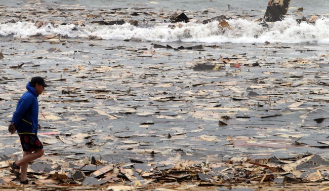 A man passes by driftwood floating toward Haeundae Beach in Busan on Monday, in the aftermath of Typhoon Nakri.   Yonhap