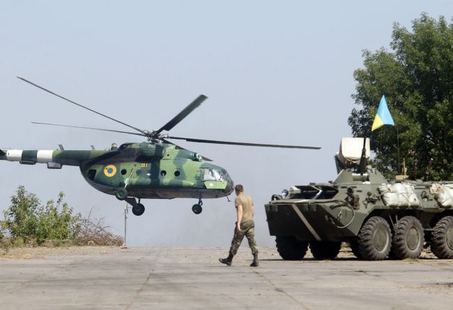 A serviceman walks near an armored personnel carrier while a helicopter flies on the position of the Ukrainian troops in Donetsk region Saturday.   AFP-Yonhap