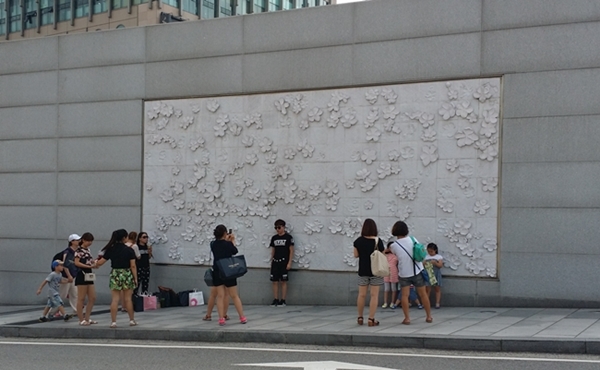 Chinese tourists posing for photographs against the famous pear blossom engraving wall on Ewha Womans University campus during the peak 2010s tourism boom that later collapsed after the 2016 THAAD dispute