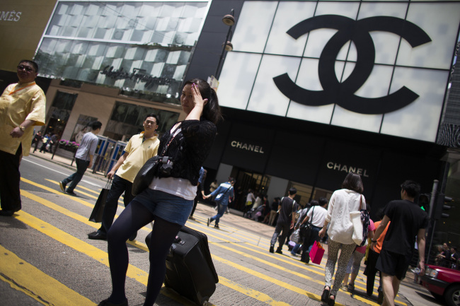Pedestrians and shoppers cross the street in front of a Chanel store in the Tsim Sha Tsui area of Hong Kong.   Bloomberg