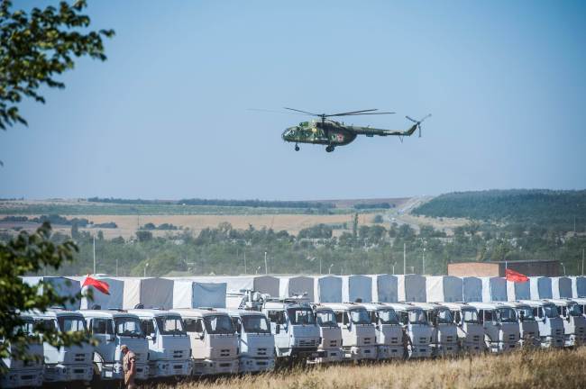 A Russian military helicopter flies over the trucks of Russian humanitarian convoy at a field outside the town of Kamensk-Shakhtinsky in Rostov region, Russia, Friday.   AFP-Yonhap