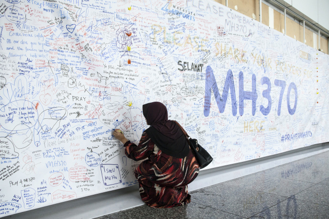 A woman writes a message on a banner for missing Malaysian Airline System Bhd. Flight 370 at Kuala Lumpur International Airport in Sepang, Malaysia, March 14. (Bloomberg)