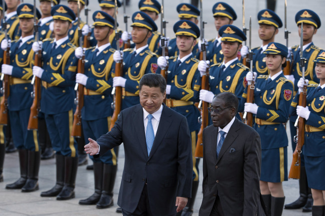 Chinese President Xi Jinping (left) shows Zimbabwe’s President Robert Mugabe the way during a welcome ceremony outside the Great Hall of the People in Beijing on Monday.   AP-Yonhap
