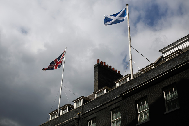 A Union flag (left), the national flag of the United Kingdom, and a St. Andrew’s or Saltire flag, the national flag of Scotland, fly from flagpoles above buildings in Downing Street in London on Wednesday.   Bloomberg