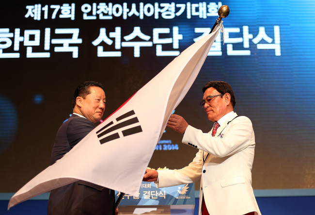 Korean Olympic Committee president Kim Jung-haeng (left) hands over the flag of the South Korean delegation to the Incheon Asian Games chief delegate Park Soon-ho in a ceremony in Seoul on Thursday. South Korea hopes to finish second in the medal standings for the fifth straight time at the 17th Asian Games, to be held from Sept. 19 to Oct. 4.    Yonhap