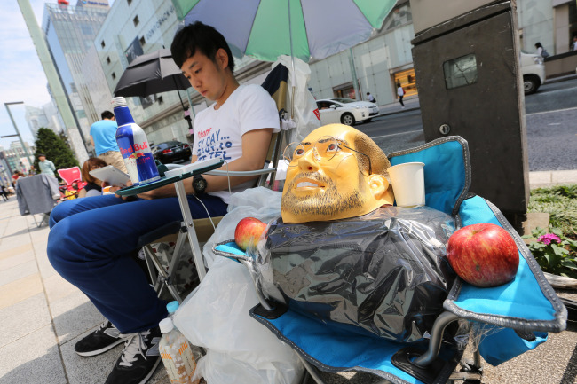A man uses an iPad while sitting next to a mask resembling the late Apple Inc. cofounder Steve Jobs as he waits in line outside the Apple Store Ginza ahead of the launch of the company’s new iPhone 6 and iPhone 6 Plus in Tokyo on Friday.   Bloomberg