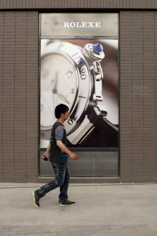 A pedestrian walks past a sign depicting counterfeit Rolex watches in Xi’an, Shaanxi province, China.   Bloomberg
