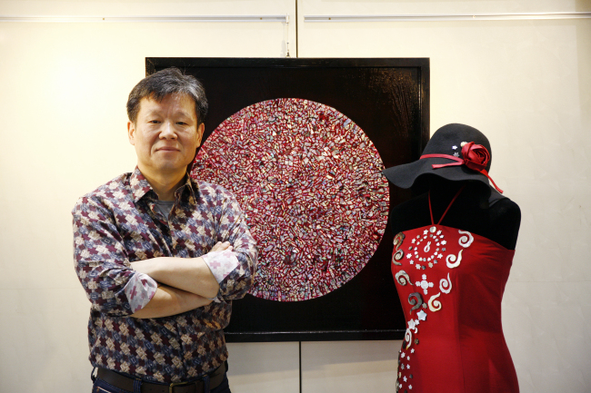 Artist Kim Young-jun poses in front of his lacquer painting inlaid with colorful mother-of-pearl and a collaborative dress with a fashion designer at his exhibition in Seoul.    Courtesy of the artist