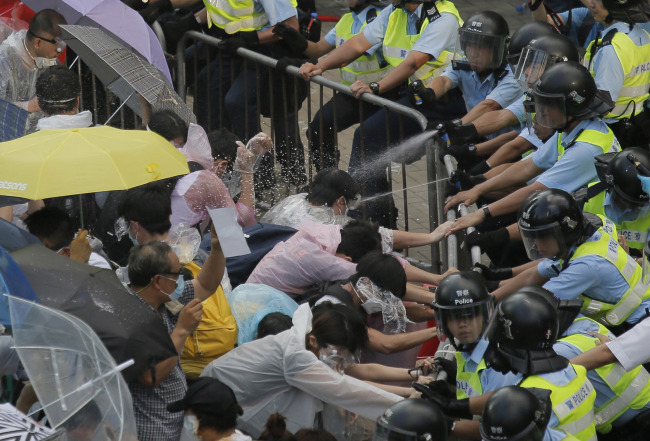 Riot police use pepper spray against protesters after thousands of people block a main road to the financial Central district outside the government headquarters in Hong Kong on Sunday.   AP-Yonhap