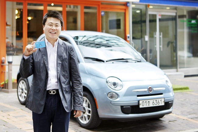SoCar CEO Kim Ji-mahn poses against the backdrop of  the company-owned Fiat 500, a tiny Italian car, while presenting a membership card used for the firm’s car sharing service in Seoul.    SoCar