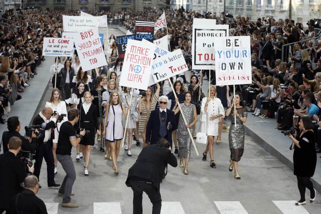 Fashion designer Karl Lagerfeld (center) acknowledges the public along with models faking a demonstation as they present creations for Chanel during the 2015 spring-summer ready-to-wear collection fashion show on Tuesday at the Grand Palais in Paris.   AFP-Yonhap