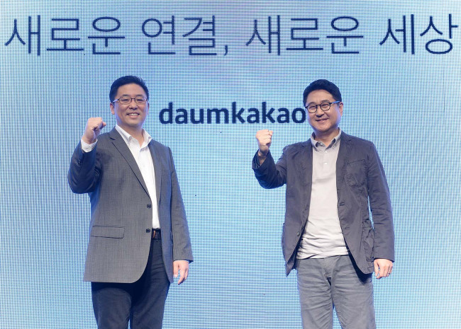 Daum Kakao CEOs Choi Sae-hoon (left) and Lee Sir-goo pose for a photo in front of a new corporate logo at a launch event in Seoul on Wednesday.   Daum Kakao