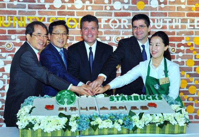 Jeff Hansberry (second from right), president of Starbucks China and Asia Pacific; John Culver (third from right), group president of China and Asia Pacific for channel development and emerging brands; Lee Seock-koo (second from left), Starbucks Korea CEO, and others cut a cake to mark the opening of the first Starbucks Community Store in Seoul on Wednesday.    Starbucks Korea